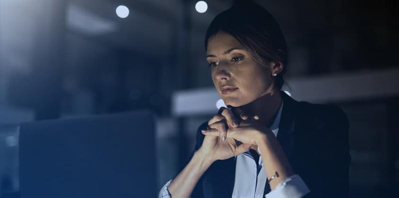Professional woman working at computer sitting at a desk in a dimly lit office environment