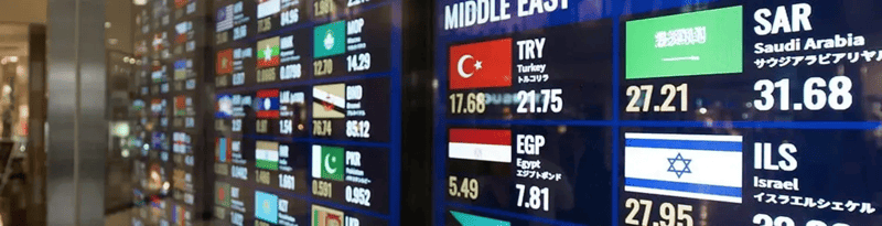 Digital screens showing multiple international currency exchange rates with country flags in a financial or airport setting.