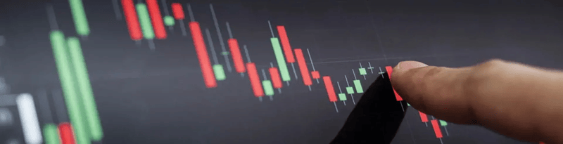Close-up of a finger pointing at a digital candlestick chart on a screen, highlighting changes in price movement