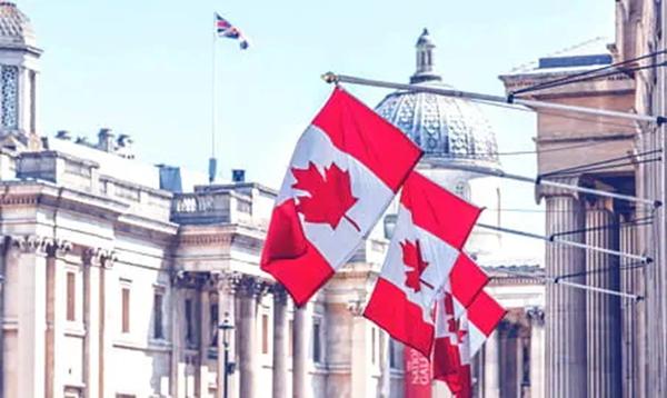 Canadian flags displayed on flagpoles in front of historic city buildings with domed architecture