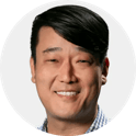 Portrait of a smiling person with short dark hair wearing a striped light-colored shirt on a white background
