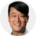 Portrait of a smiling person with short dark hair wearing a striped light-colored shirt on a white background