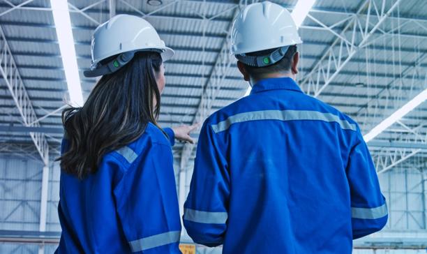 Two workers wearing safety helmets and protective uniforms examining the interior of an industrial facility