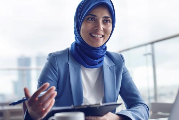 Person wearing a blue headscarf and blue blazer holding a clipboard during a meeting.