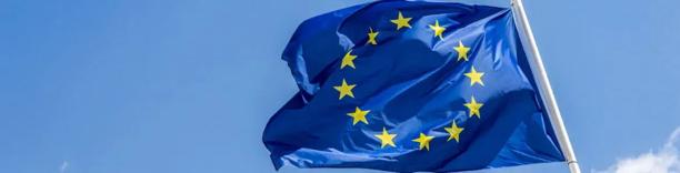 European Union flag with yellow stars on a blue background waving against a clear sky.