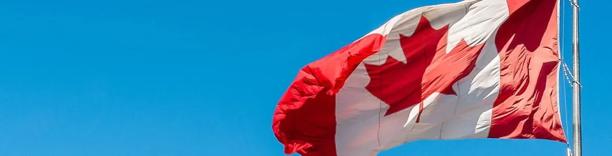 Canadian national flag with a red maple leaf waving against a clear blue sky.