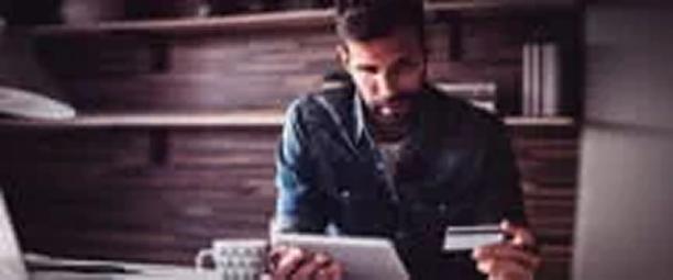Man sitting at desk holding a credit card and tablet