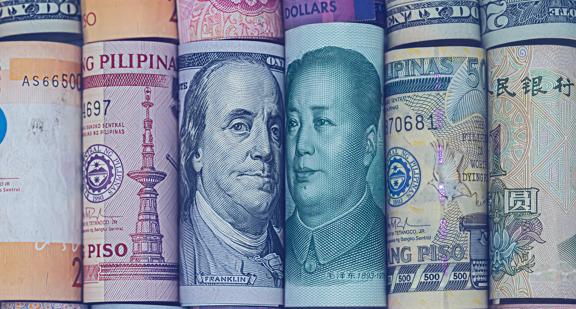 Rolled international banknotes including US dollars, Chinese yuan, and Philippine peso, showing global currencies side by side.