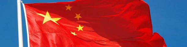 Red flag of China with five yellow stars waving against a clear blue sky.