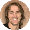 Portrait of a person with wavy hair wearing a dark top against a light brown textured background