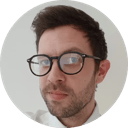Portrait of a person wearing glasses and a white shirt against a light background