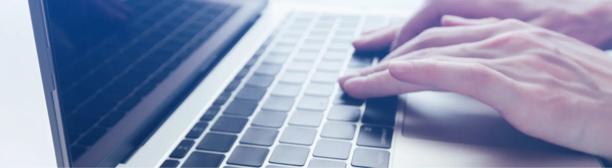 Close-up of hands typing on a laptop keyboard with a blurred screen in the background. The image represents digital work and online communication.