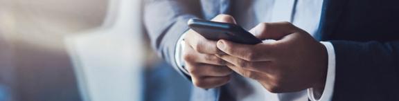 Close-up of hands holding a smartphone. The person is wearing a formal suit and using the phone for communication.