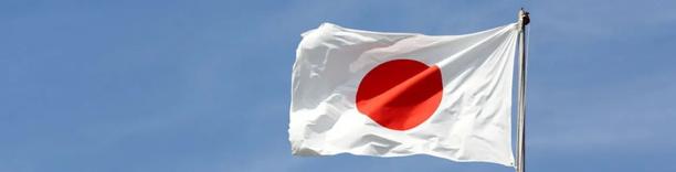 Japanese national flag with a red circle on a white background waving against a clear blue sky.