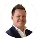 Professional headshot of a person with short styled hair in a dark suit jacket and white shirt on a white background
