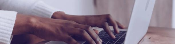 Close up of hands typing on a laptop keyboard on a wooden desk