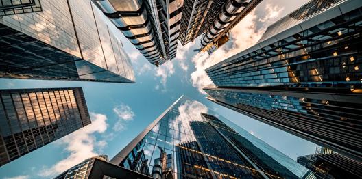 Upward view of modern skyscrapers in a financial district with glass facades reflecting clouds and blue sky.