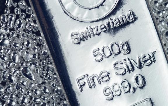 Close-up of a 500g fine silver bar from Switzerland with 999.0 purity, surrounded by metallic granules.