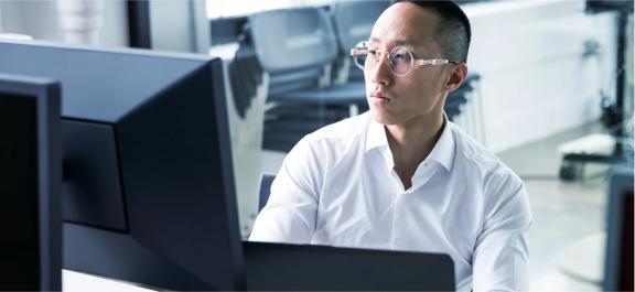 Individual in a white shirt working on multiple computer monitors in a modern office setting