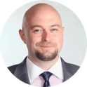 Portrait of a bald man with a short beard wearing a suit, dress shirt, and tie against a plain white background.