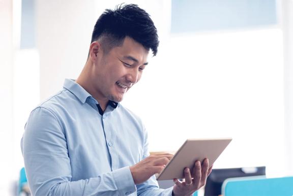Person wearing a light blue shirt using a tablet device in a bright modern office environment with blurred background elements.