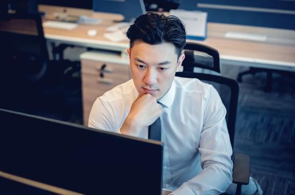 Person in formal attire seated at an office desk working on a computer monitor in a modern workspace.