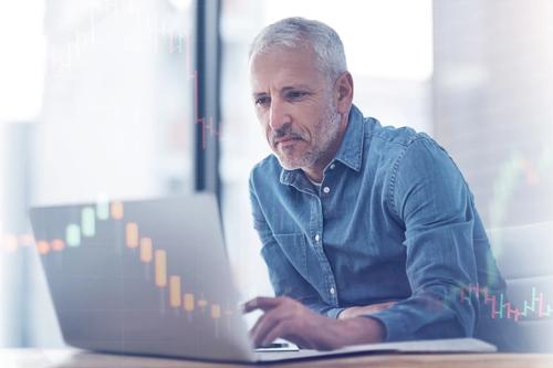 Mature man analyzing stock market data on a laptop with digital candlestick chart overlay